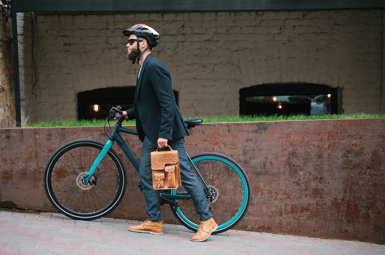 Ein Mann im Businessoutfit schiebt sein blaues Fahrrad